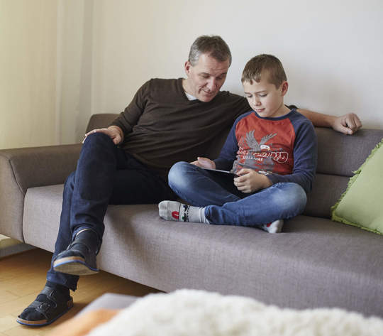Vater und Sohn sitzen auf dem Sofa und schauen auf das Tablet